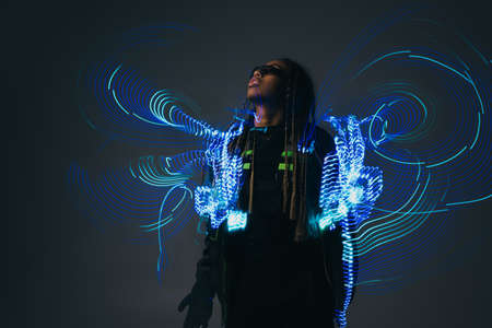 Stylish african american woman in smart glasses standing near abstract projection on grey background