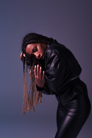 Trendy african american woman in leather jacket posing isolated on purple