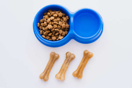 top view of bone shaped pet treats near bowl with water and dry pet food isolated on white