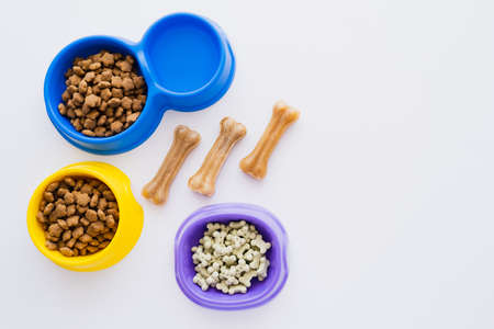 top view of bone shaped pet treats near bowls with water and dry pet food isolated on whiteの写真素材