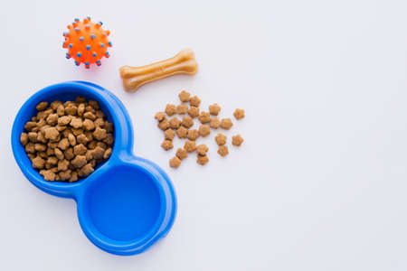 top view of bone shaped pet treat near bowl with dry pet food and rubber toy isolated on whiteの写真素材