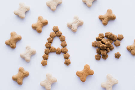 top view of bone shaped pet treats near letter and dry pet food isolated on white