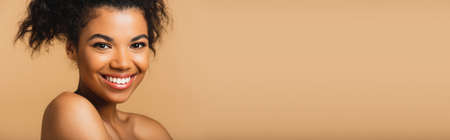 portrait of cheerful african american woman with bare shoulders and perfect skin isolated on beige, bannerの写真素材