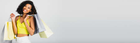 happy african american woman holding shopping bags and credit card isolated on grey, bannerの写真素材