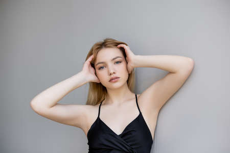 Stylish young woman touching hair and looking at camera on grey backgroundの写真素材