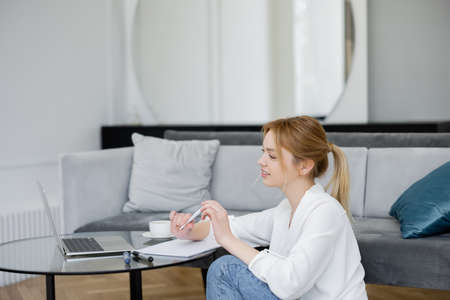 Young freelancer looking at laptop near cup and notebook at home