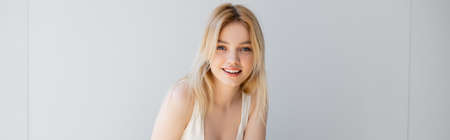 Portrait of blonde woman smiling at camera near grey wall, bannerの写真素材