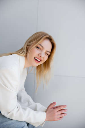 Blonde woman in jacket winking at camera at home