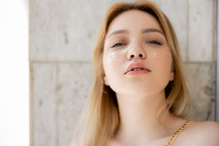 Portrait of blonde woman with glitter on cheeks looking at camera at homeの写真素材