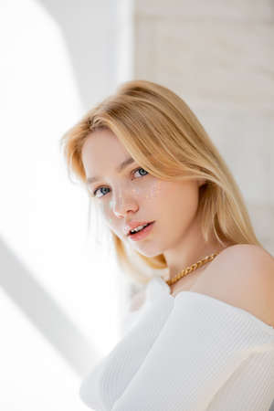 Blonde woman with glitter makeup looking at camera at homeの写真素材