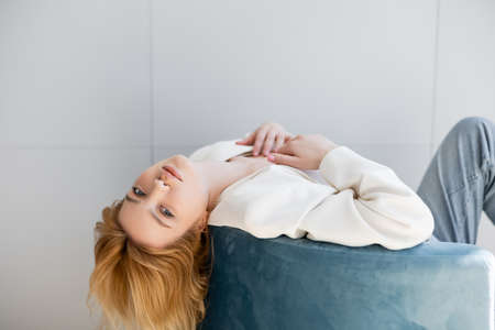 Stylish woman in jacket posing on armchair in living roomの写真素材