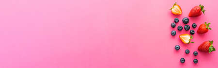Top view of organic strawberries and blueberries on pink background, banner