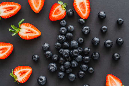 Top view of whole blueberries and cut strawberries on black backgroundの写真素材