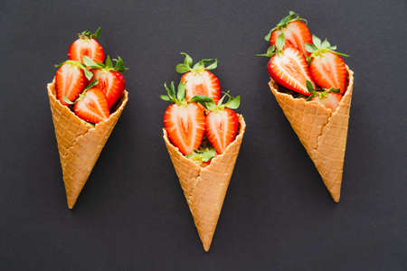 Top view of ripe cut strawberries in waffle cones on black background