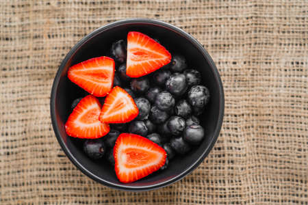Top view of organic berries in bowl on sackcloth