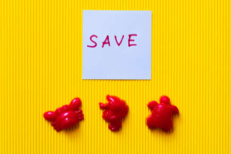 top view of toy sea animals near blue paper with save lettering on yellow background