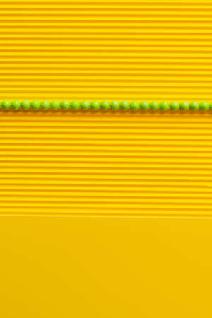 top view of green balls in horizontal row on yellow textured backgroundの写真素材