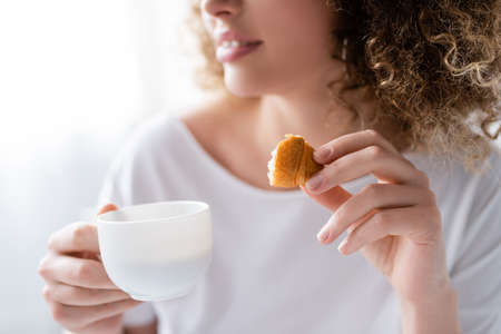 partial view of blurred woman with coffee cup and piece of delicious croissantの写真素材