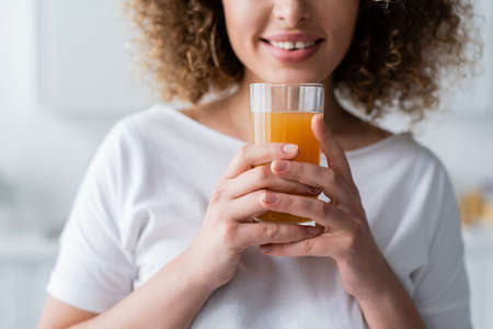 cropped view of curly smiling woman holding glass of fresh orange juiceの写真素材