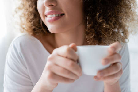partial view of smiling woman with curly hair holding white coffee cupの写真素材