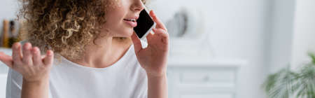 partial view of woman with curly hair talking on mobile phone at home, banner
