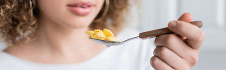 partial view of curly woman holding spoon with tasty corn flakes, bannerの写真素材