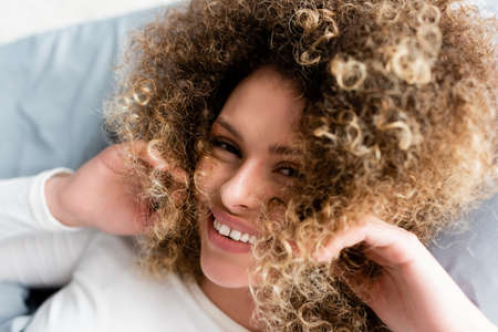 top view of cheerful woman with wavy hair near face smiling at cameraの写真素材