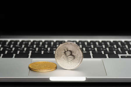 KYIV, UKRAINE - APRIL 26, 2022: Close up view of bitcoins on blurred laptop isolated on blackのeditorial素材