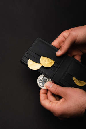 KYIV, UKRAINE - APRIL 26, 2022: Cropped view of man holding silver bitcoin and wallet isolated on blackのeditorial素材