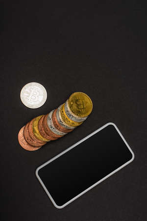 KYIV, UKRAINE - APRIL 26, 2022: Top view of crypto coins near smartphone with blank screen on black backgroundのeditorial素材