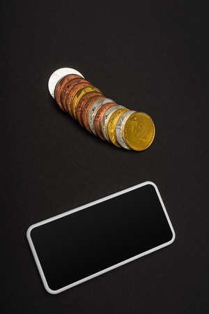 KYIV, UKRAINE - APRIL 26, 2022: Top view of mobile phone near bitcoins on black backgroundの写真素材