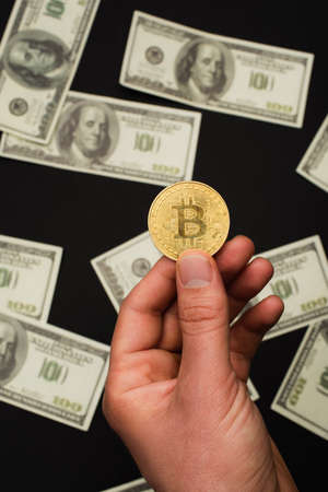 KYIV, UKRAINE - APRIL 26, 2022: Top view of man holding crypto coin near dollar banknotes on black backgroundのeditorial素材