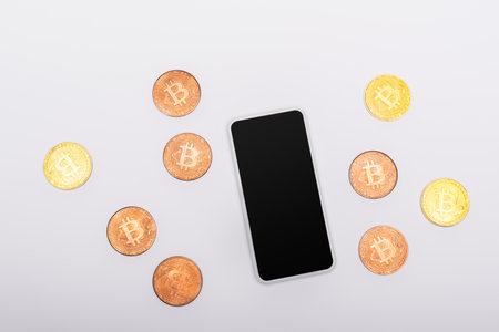 KYIV, UKRAINE - APRIL 26, 2022: Top view of cellphone with blank screen near crypto coins on white backgroundのeditorial素材