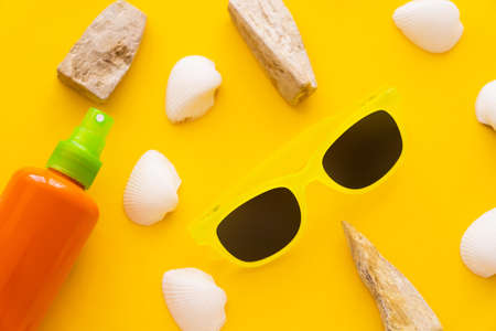 Top view of sunscreen near sunglasses and seashells on yellow background