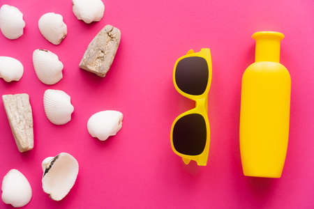 Top view of seashells near sunglasses and bottle of sunscreen on pink backgroundの写真素材