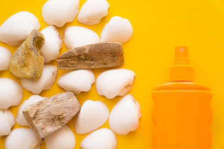 Top view of seashells and stones near sunblock on yellow background