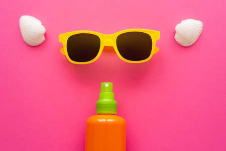 Top view of sunscreen near sunglasses and seashells on pink surface