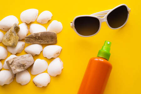 Top view of sunglasses near seashells and sunblock on yellow background