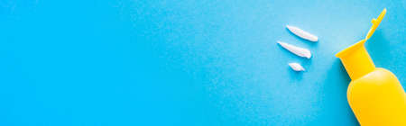 Top view of cream near bottle of sunscreen on blue background, banner