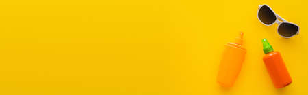 Top view of sunglasses and sunscreens on yellow background, banner