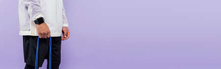 cropped view of african american man holding skipping rope isolated on purple, banner