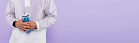 cropped view of african american man in trendy sportswear holding sports bottle isolated on purple, bannerの写真素材