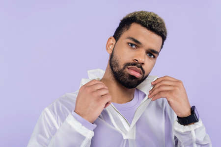 young african american sportsman with smart watch adjusting collar isolated on purple