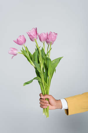 cropped view of african american man holding bouquet of pink tulips isolated on greyの写真素材