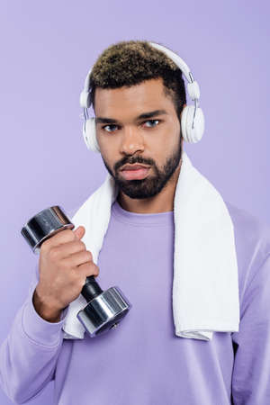 bearded african american man in headphones exercising with dumbbell isolated on purpleの写真素材