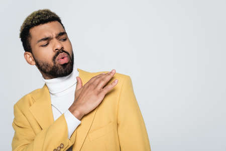 young african american man in yellow blazer and polo neck dust off shoulder isolated on greyの写真素材