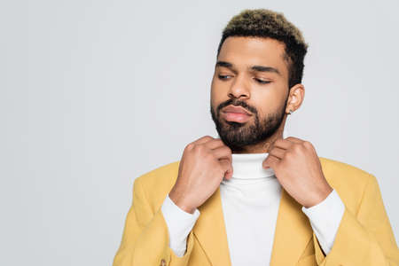 bearded african american man in stylish blazer adjusting polo neck isolated on greyの写真素材