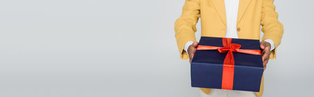 cropped view of african american man in yellow stylish blazer holding wrapped present isolated on grey, bannerの写真素材