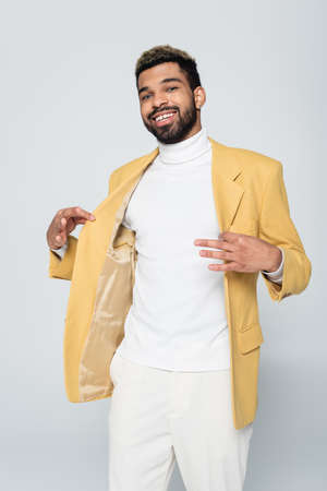 cheerful african american man adjusting yellow blazer isolated on greyの写真素材