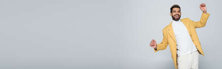 excited african american man in stylish yellow blazer posing isolated on grey, bannerの写真素材